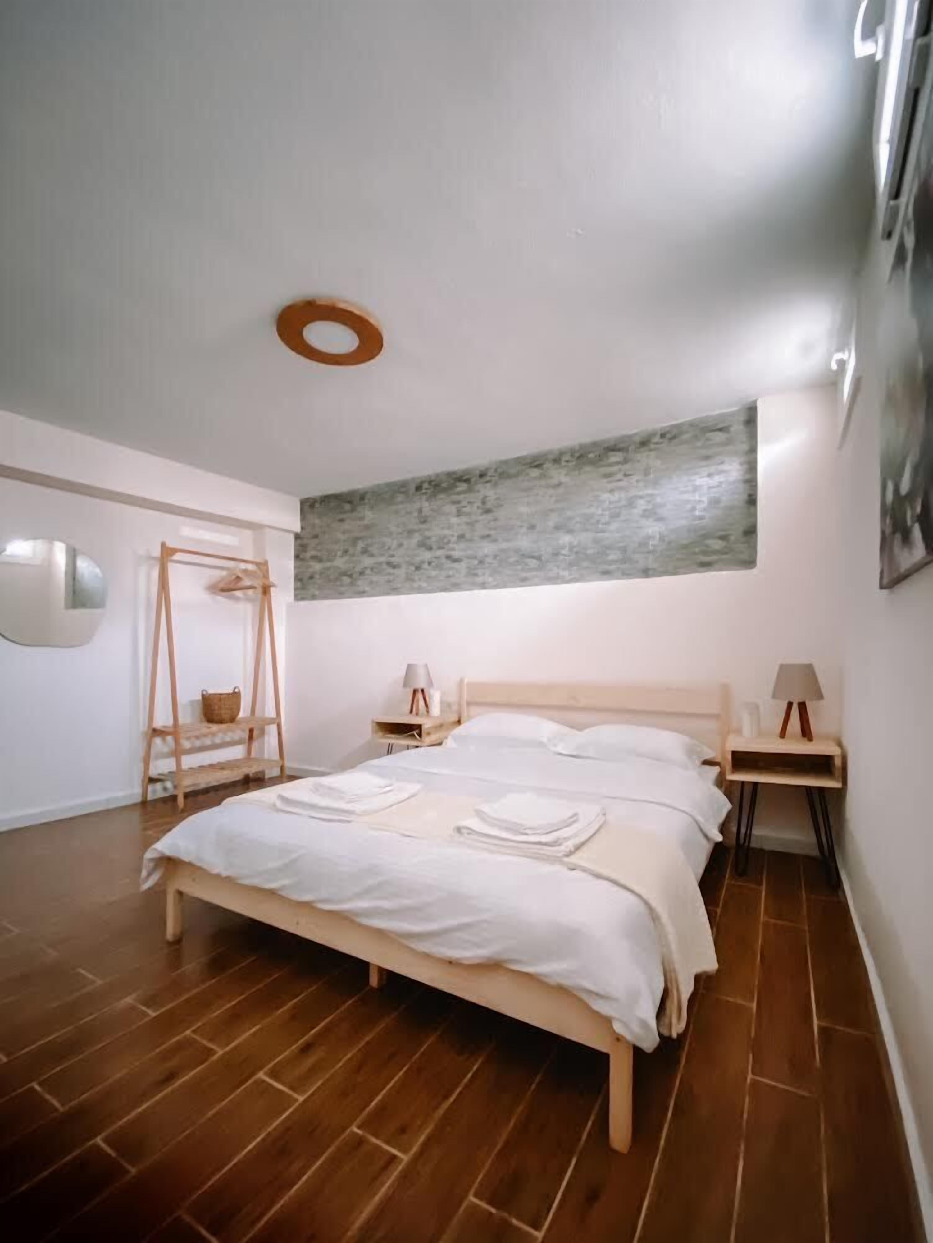 A bedroom with a wooden bed, two bedside tables with lamps, a hanging basket, and a large abstract painting on the wall.