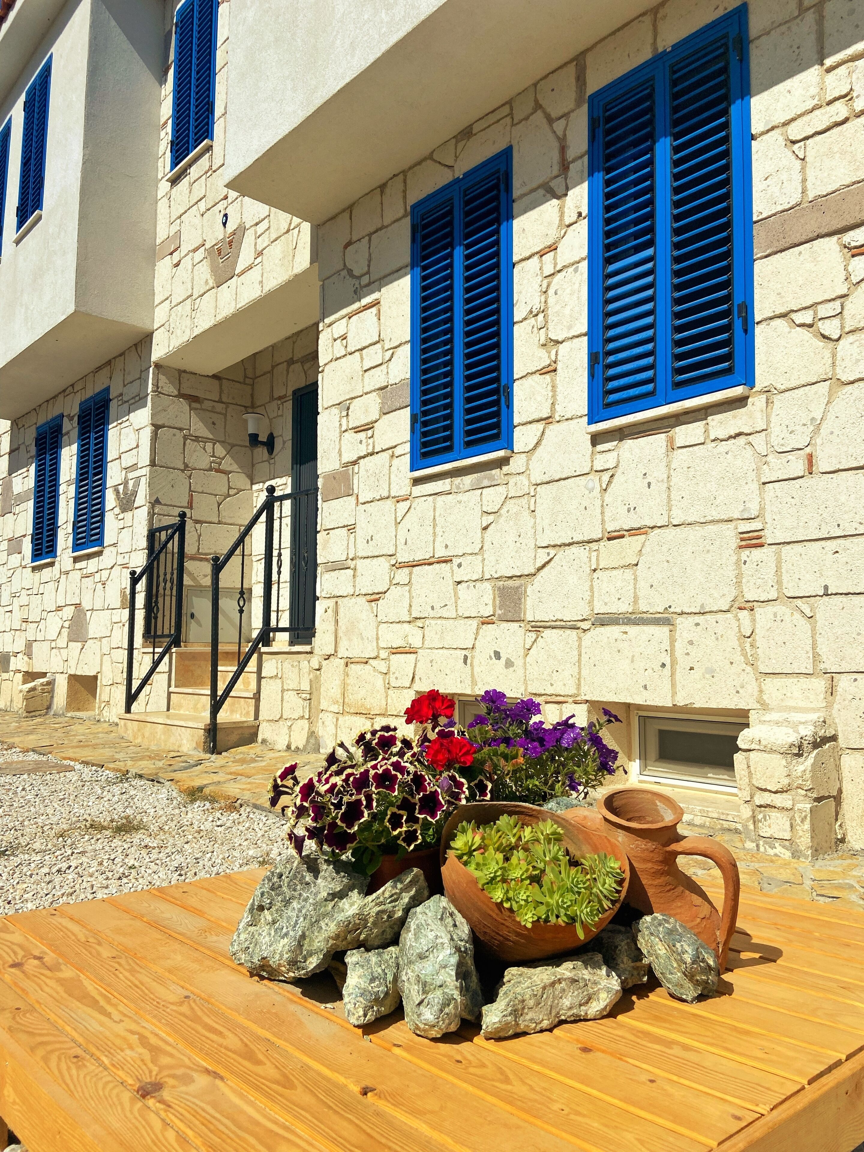 A stone building with blue shutters and a wooden table with potted plants and rocks.