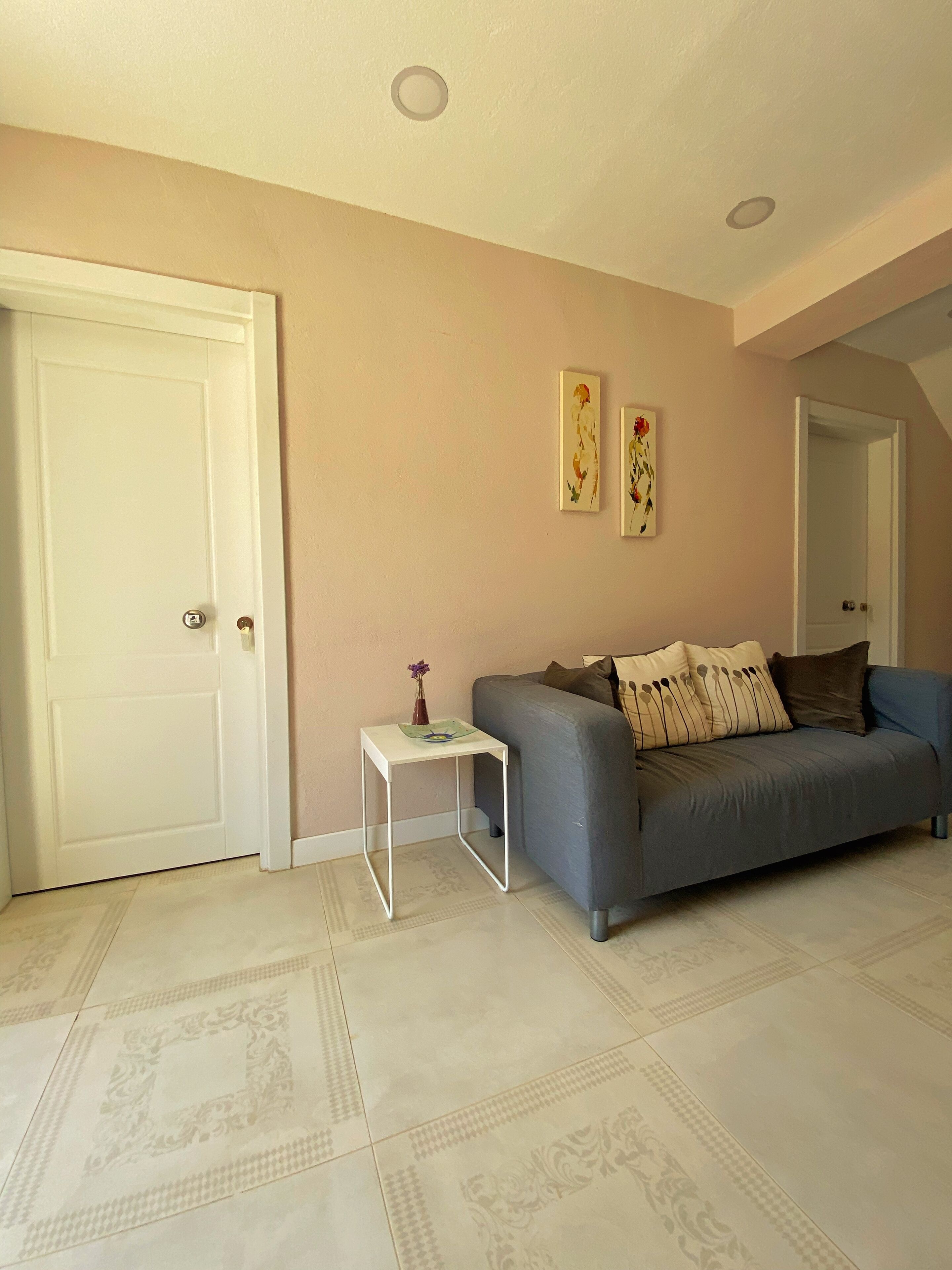 A living room with a grey sofa, a small white side table, and two wall-mounted paintings.