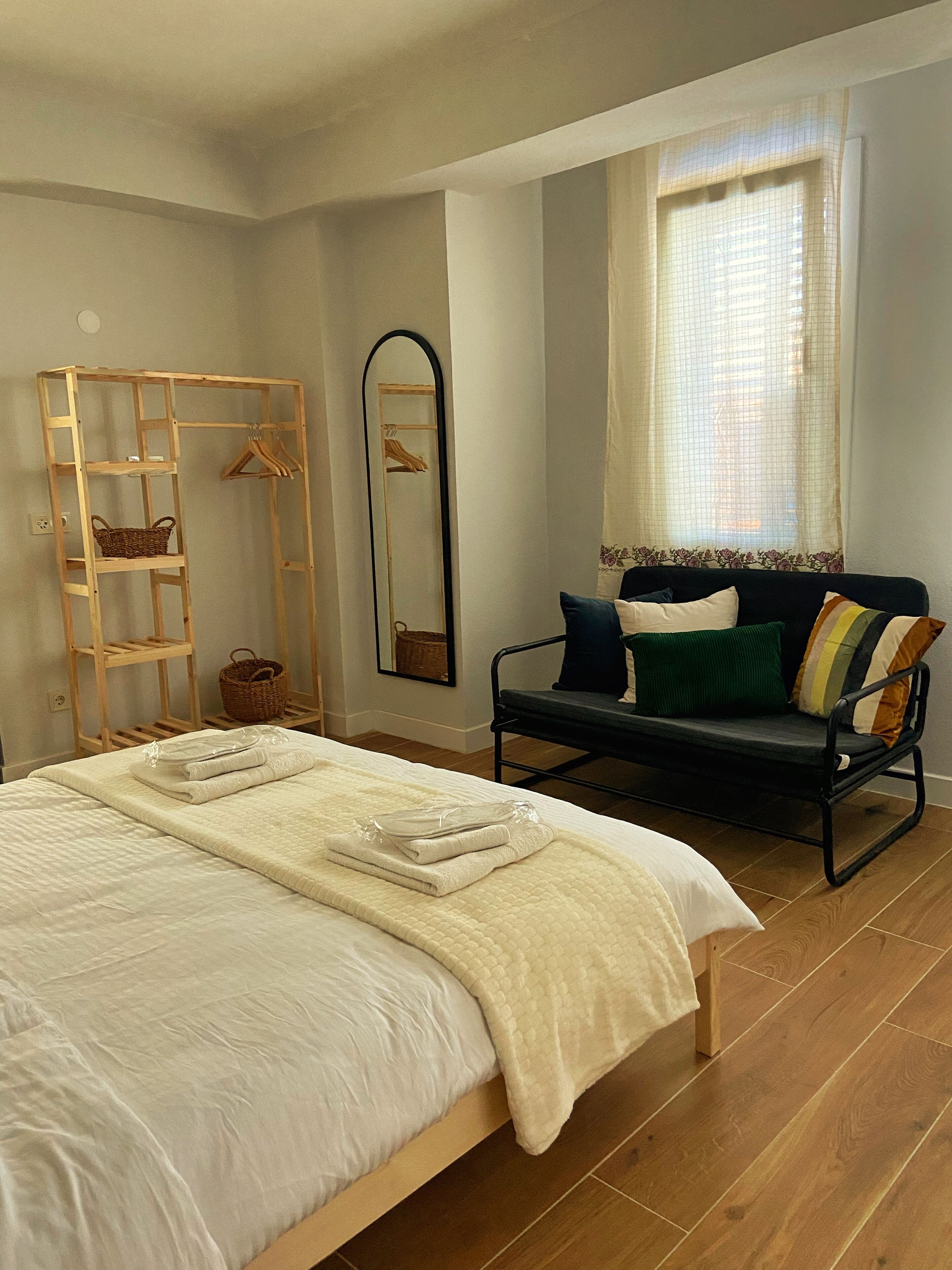 A bedroom with a bed, a wooden ladder, a mirror, a sofa, and a window with curtains.