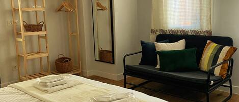 A bedroom with a bed, a wooden ladder, a mirror, a sofa, and a window with curtains.