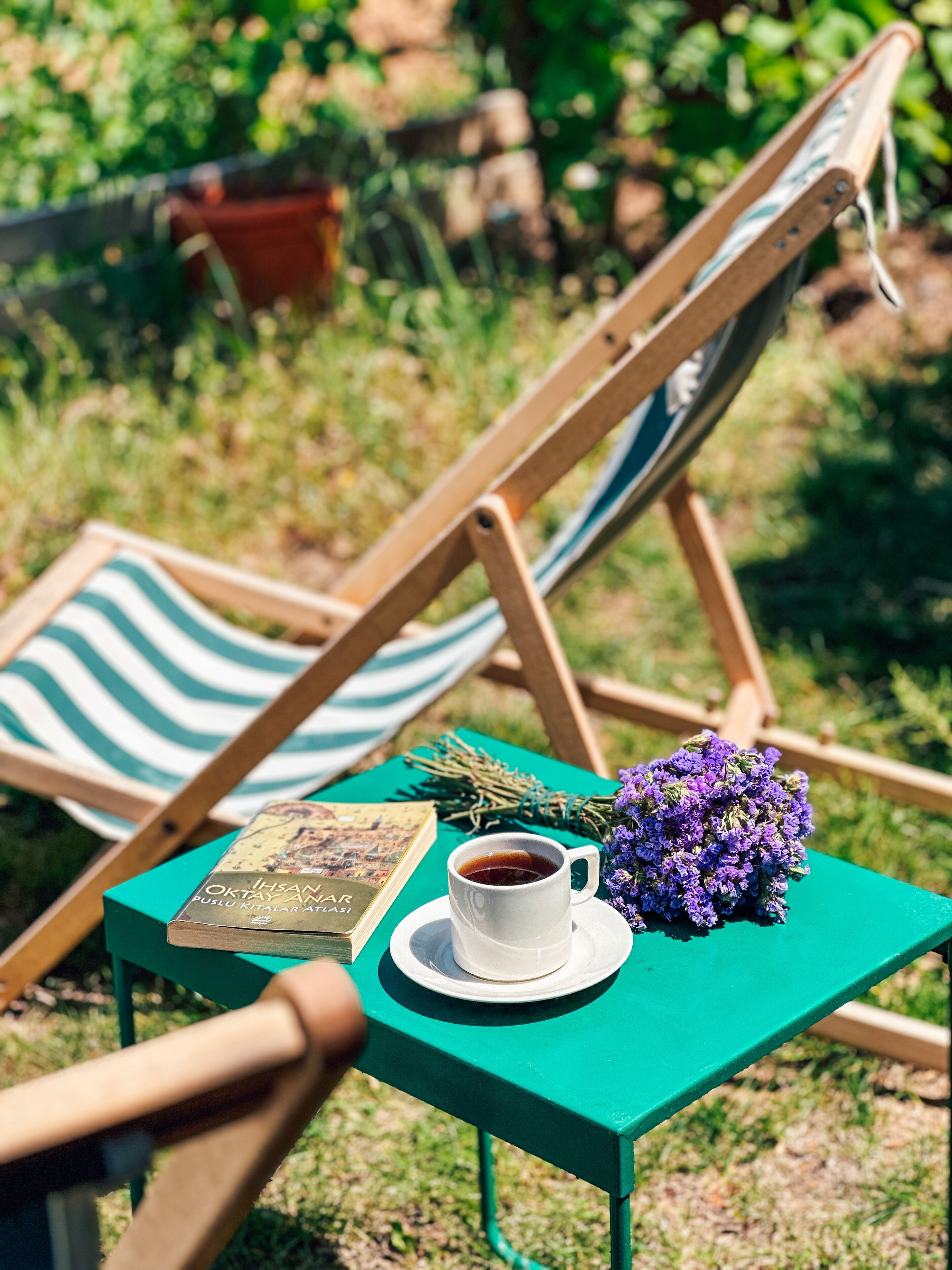 A green table with a book, a cup of coffee, and a bouquet of purple flowers.