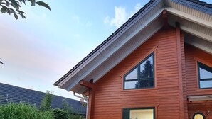 A two-story wooden house with a sloped roof, a front porch, and a brick foundation. - Gästewohnung Storchennest (Teichland)