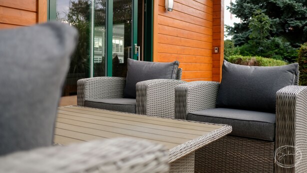 A wicker sofa with grey cushions, a wooden table, and a glass door leading to a garden. - Gästewohnung Storchennest (Teichland)