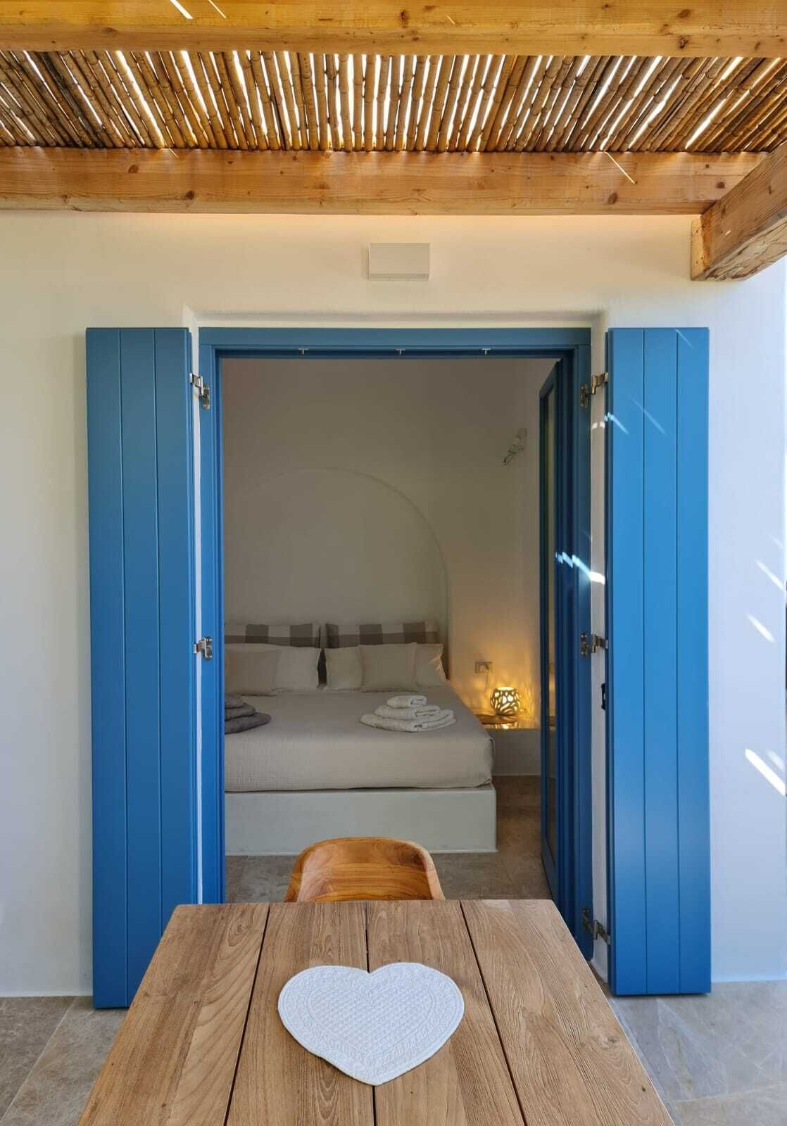 A room with a bed, a table with a heart-shaped placemat, and blue doors leading to another room.