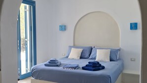A bedroom with a bed, blue bedding, a white headboard, and a large arched doorway. - Tilos Villa (Tilos)