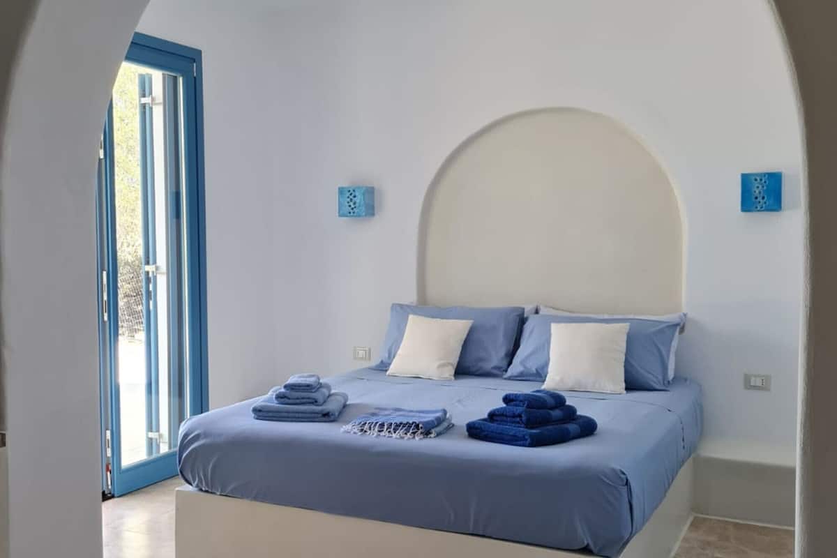 Un dormitorio con cama, ropa de cama azul, cabecera blanca y un amplio arco de entrada.