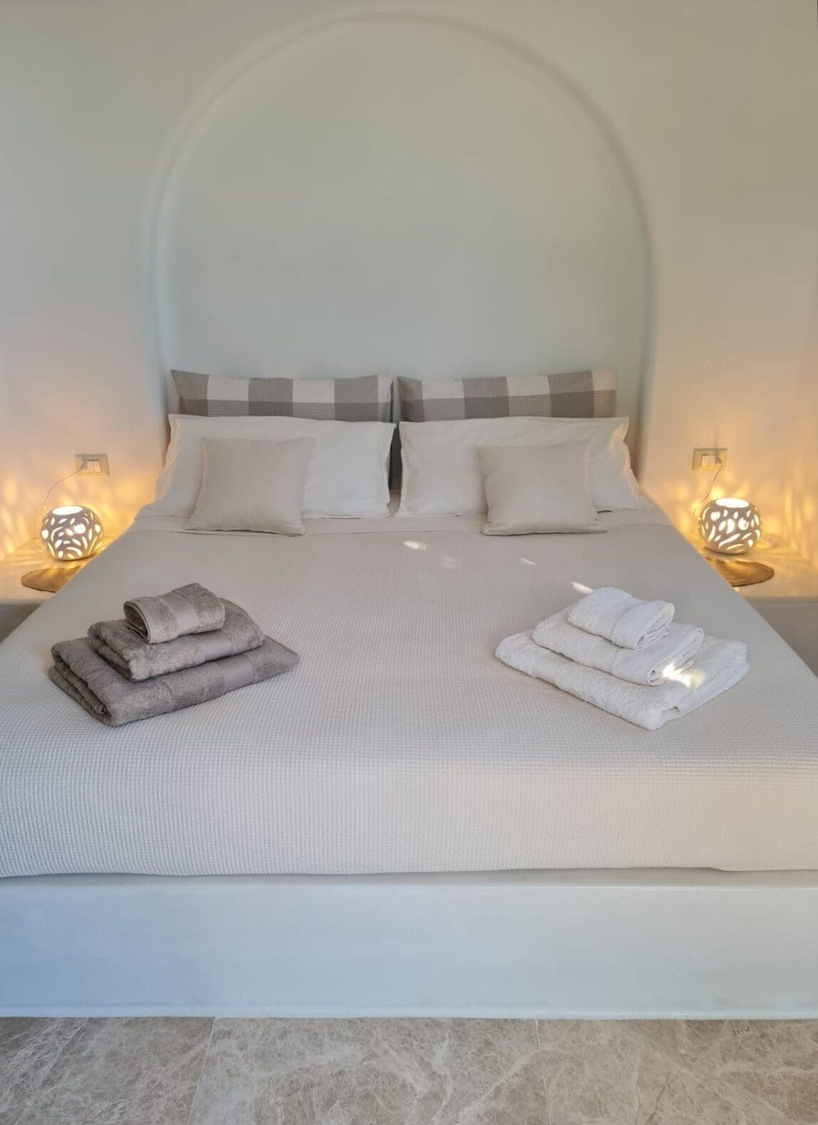 A neatly made bed with pillows and folded towels, two bedside lamps, and a marble floor.