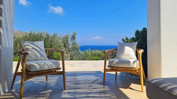 Two wicker chairs with white cushions on a balcony overlooking a scenic view of the sea and greenery. - Tilos Villa (Tilos)