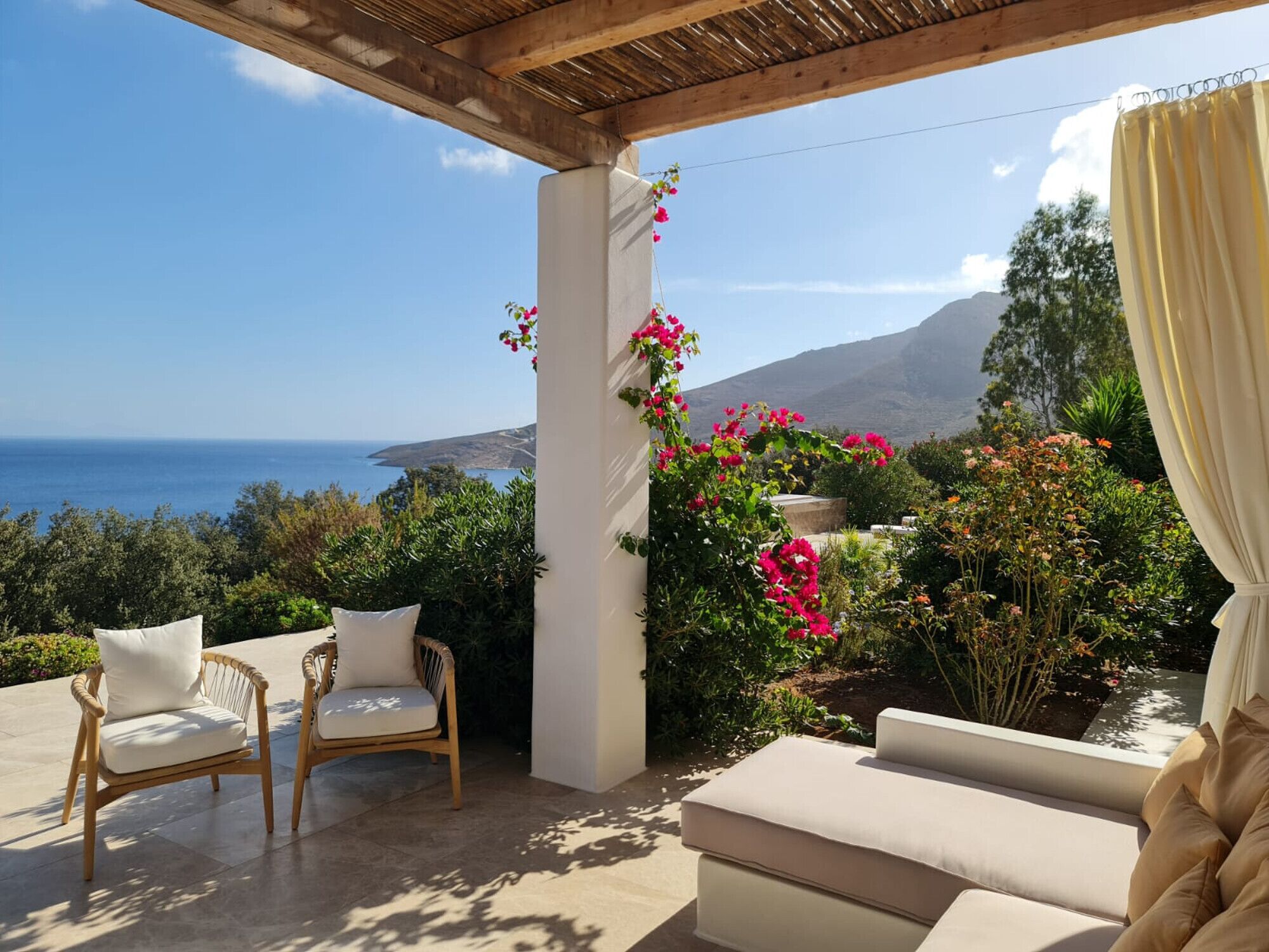 A covered outdoor seating area with a view of the sea and mountains.
