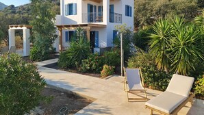 A two-story building with a balcony, surrounded by lush greenery and a mountainous backdrop. - Tilos Villa (Tilos)