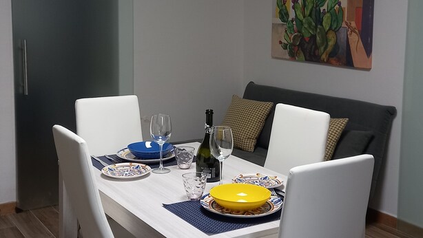 Un coin repas avec une table dressée pour deux personnes, une bouteille de vin et un tableau accroché au mur.