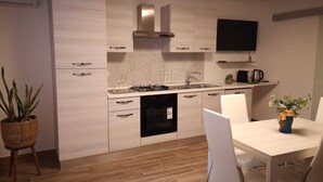 Une cuisine moderne avec des meubles de couleur bois clair, une cuisinière à gaz, un four encastré et un téléviseur à écran plat placé au-dessus du plan de travail.