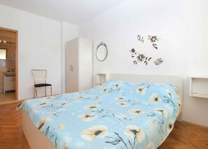 Un dormitori amb un llit, una cadira, un armari i un mirall a la paret.