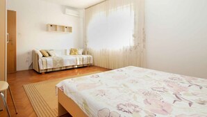 Una camera da letto con un letto, una sedia, una finestra con tende e uno scaffale a parete.