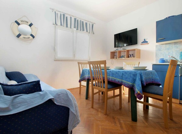Una habitació amb un llit, una taula de dinar amb cadires, una televisió i una zona de cuina.