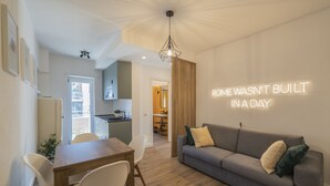 A modern living room with a grey sofa, wooden dining table, and chairs. A neon sign on the wall reads "ROME WASN'T BUILT IN A DAY". - Vintage Apartment Cipro (Rome)