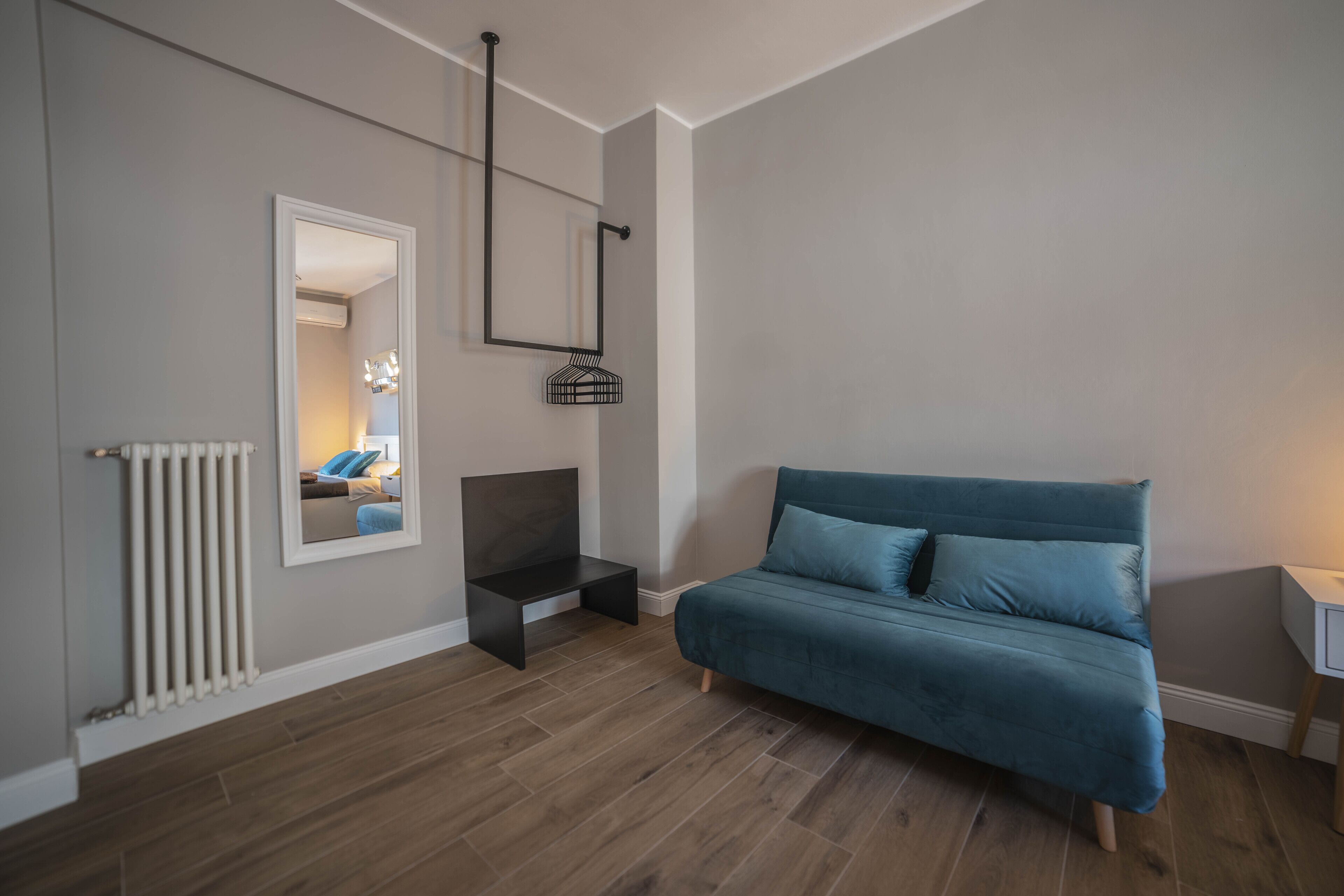 Et moderne soveværelse med blå sofa, et natbord, et spejl og en radiator.