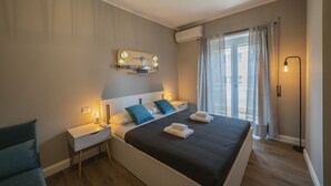 A modern hotel room with a large bed, bedside tables, a wall-mounted light fixture, and a window with curtains. - Vintage Apartment Cipro (Rome)