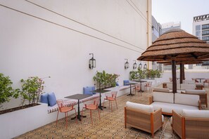 An outdoor seating area with tables, chairs, and a thatched umbrella. - Shada Hotel Dubai (Dubai)