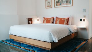 Une chambre moderne avec un cadre de lit en bois, une literie blanche et un tapis à motifs bleus.