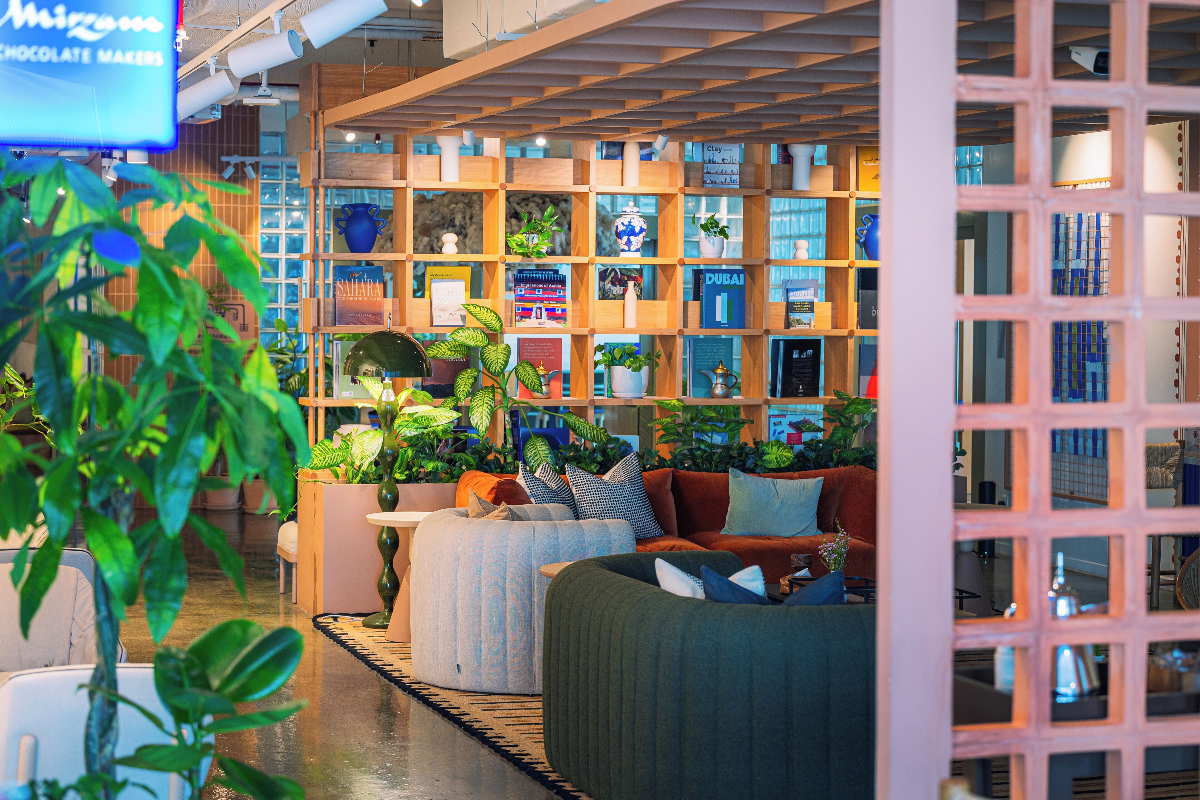 Un interior acogedor con una estantería de madera, asientos cómodos y varias plantas.