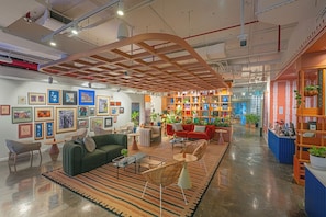 Un intérieur moderne avec un espace salon central, une bibliothèque remplie d’objets décoratifs et des œuvres d’art encadrées accrochées aux murs.