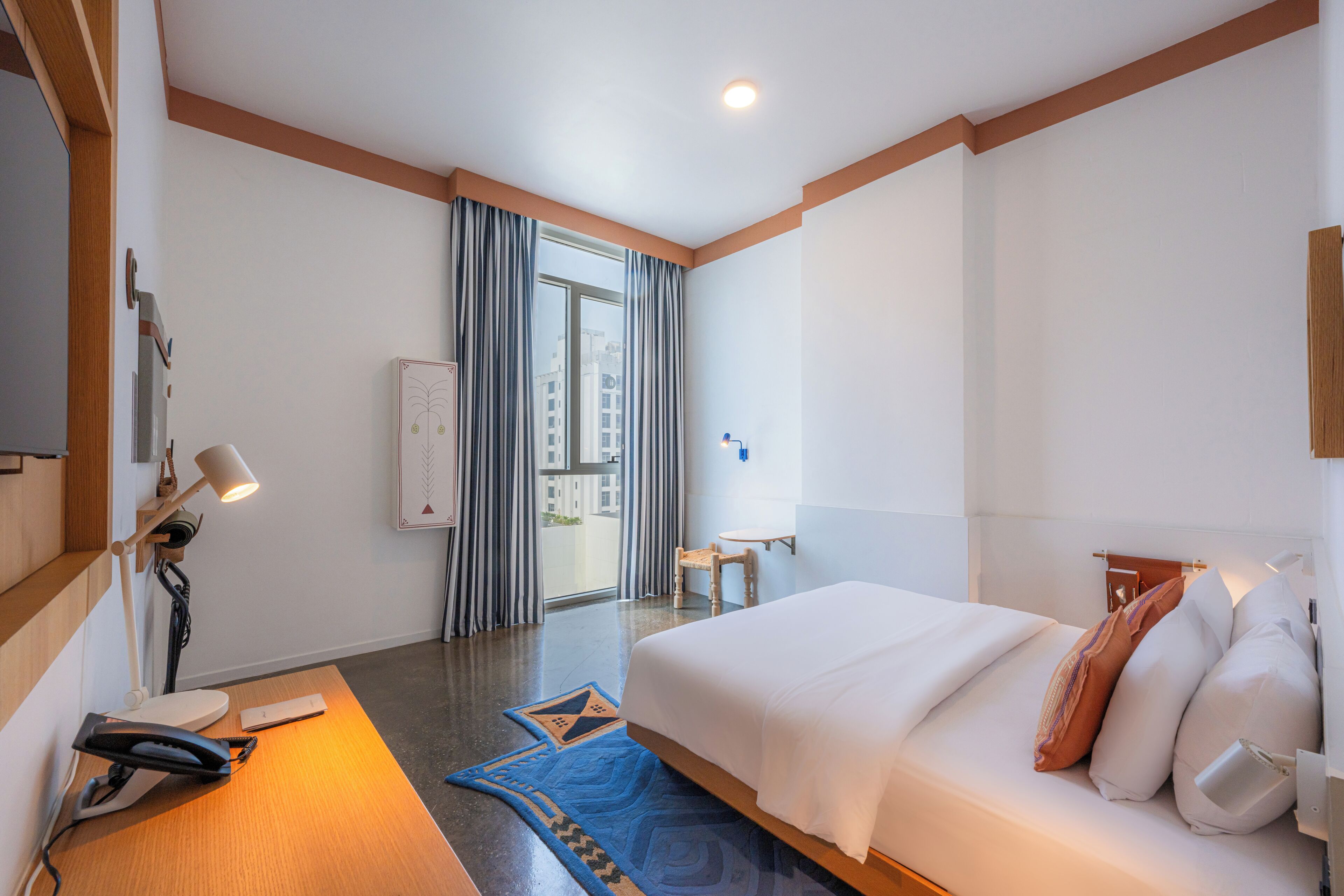 Une chambre d’hôtel avec un lit, une table de chevet, une lampe et une vue sur la ville par la fenêtre.