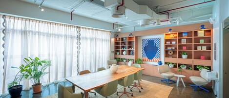 A modern meeting room with a wooden table, office chairs, a bookshelf, and potted plants.