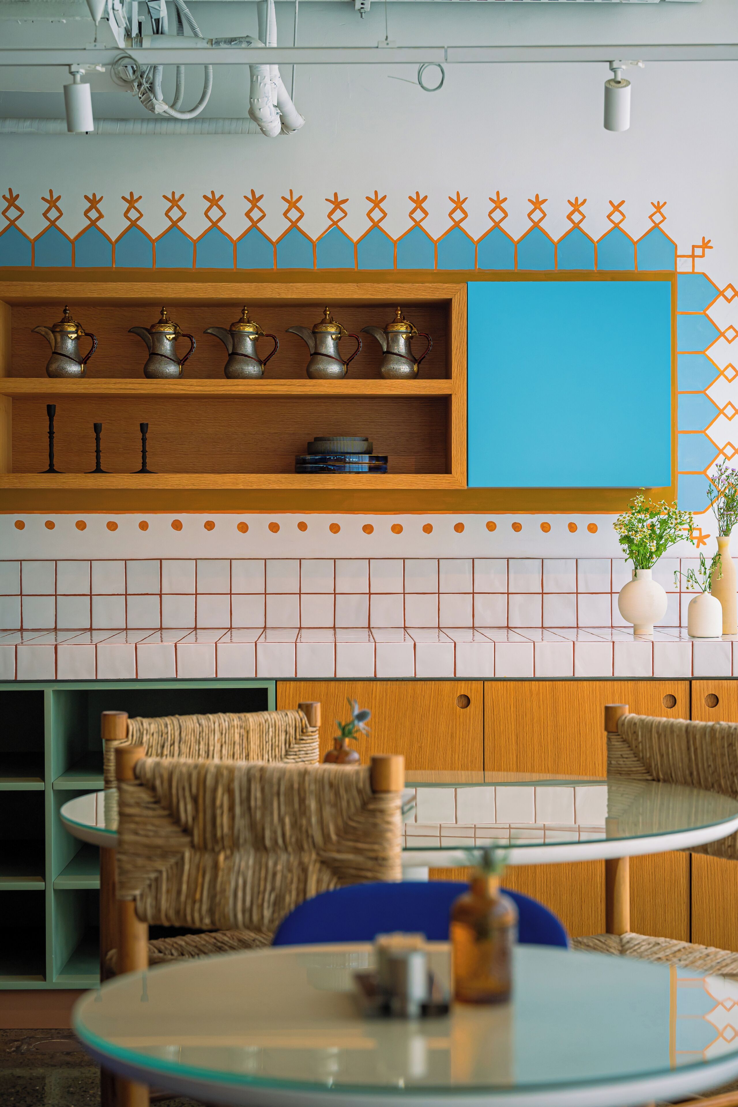 Una cocina moderna con una pared azul de acento, estantes de madera con utensilios de cocina y una mesa redonda de vidrio.