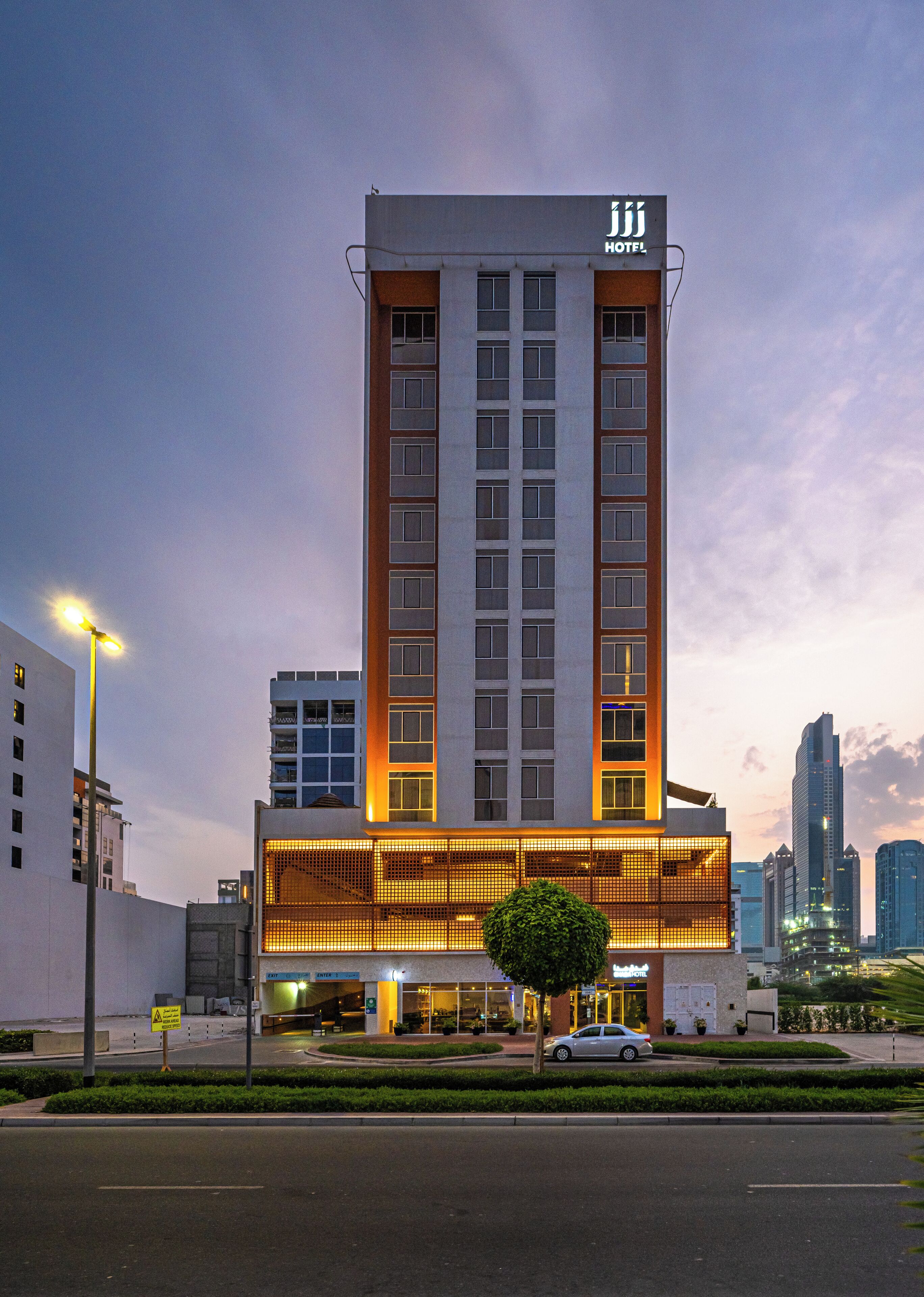 A modern hotel with a prominent entrance, multiple floors, and a city skyline in the background.