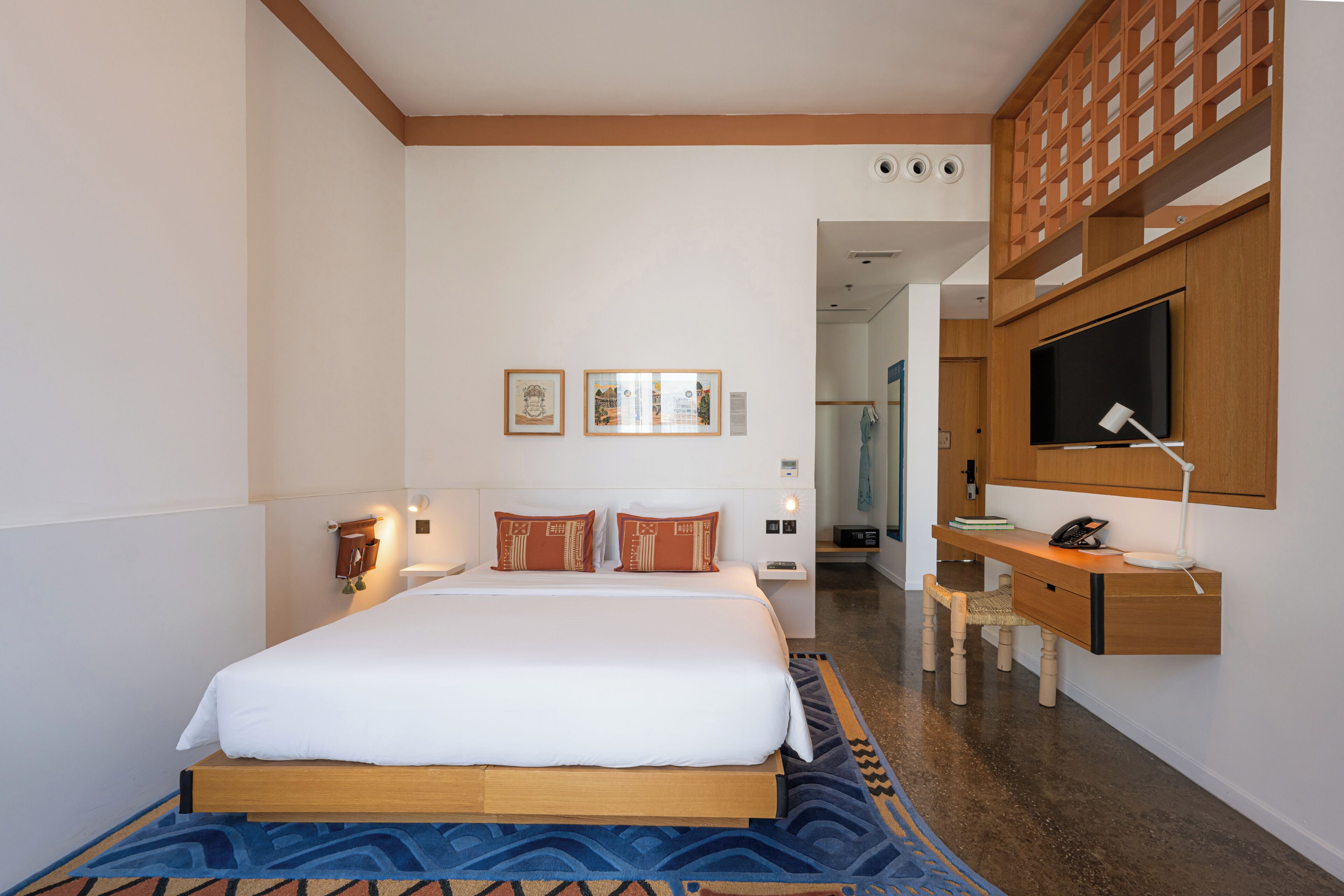 A hotel room with a large bed, a desk with a telephone, a TV mounted on the wall, and a patterned rug.