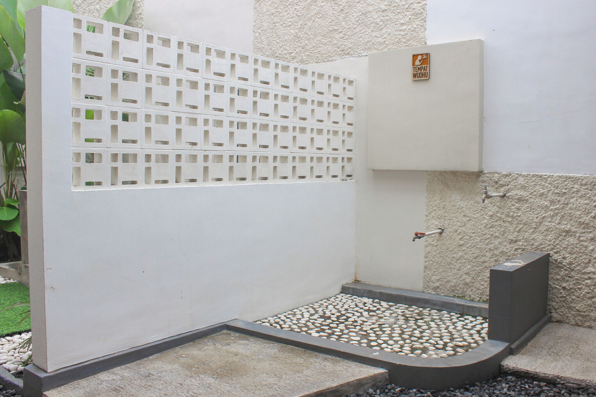 A private shower area with a white partition, pebbles on the floor, and a wall-mounted water control panel.