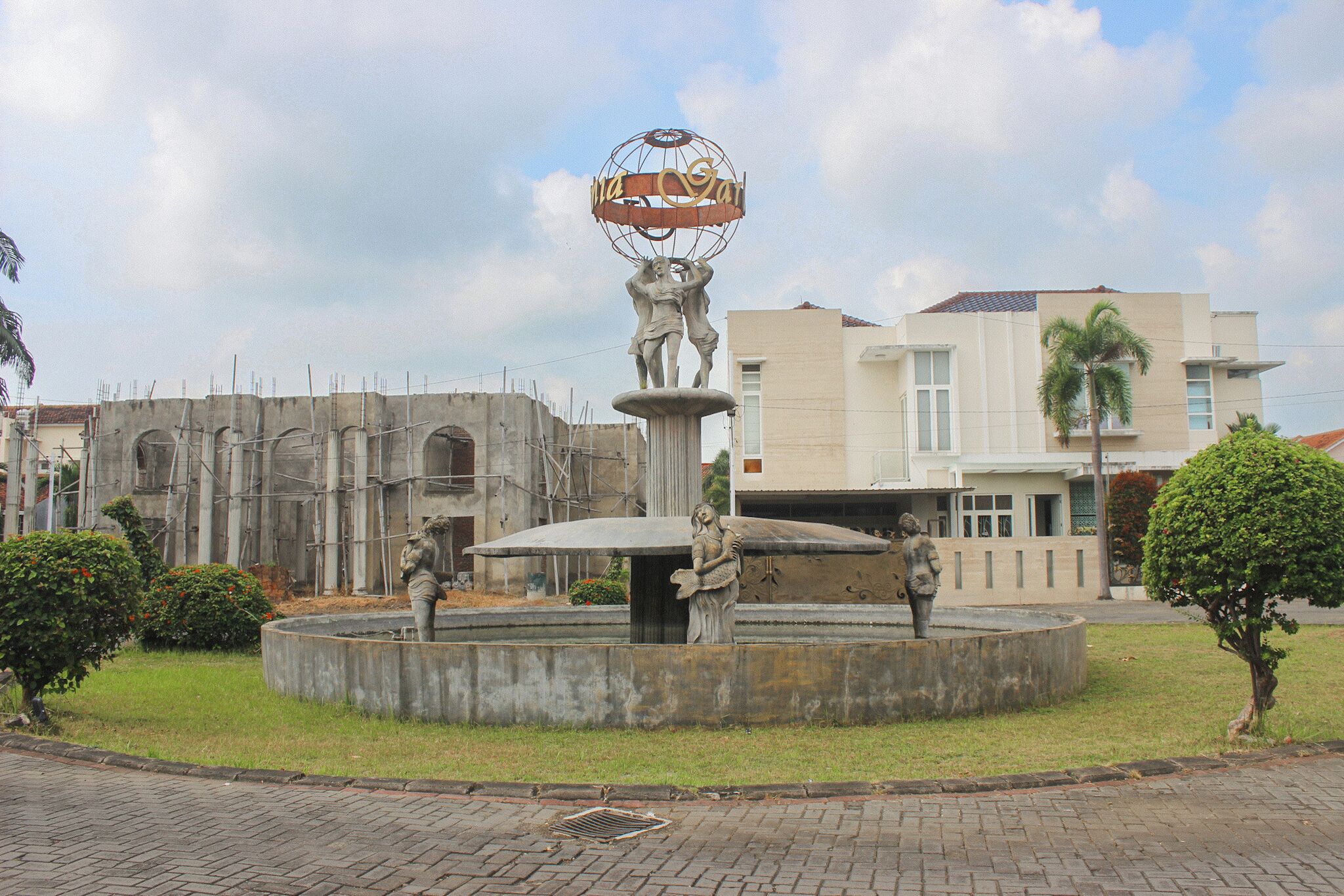 Una plaza pública con una fuente central que presenta una escultura de dos figuras sosteniendo un globo terráqueo.
