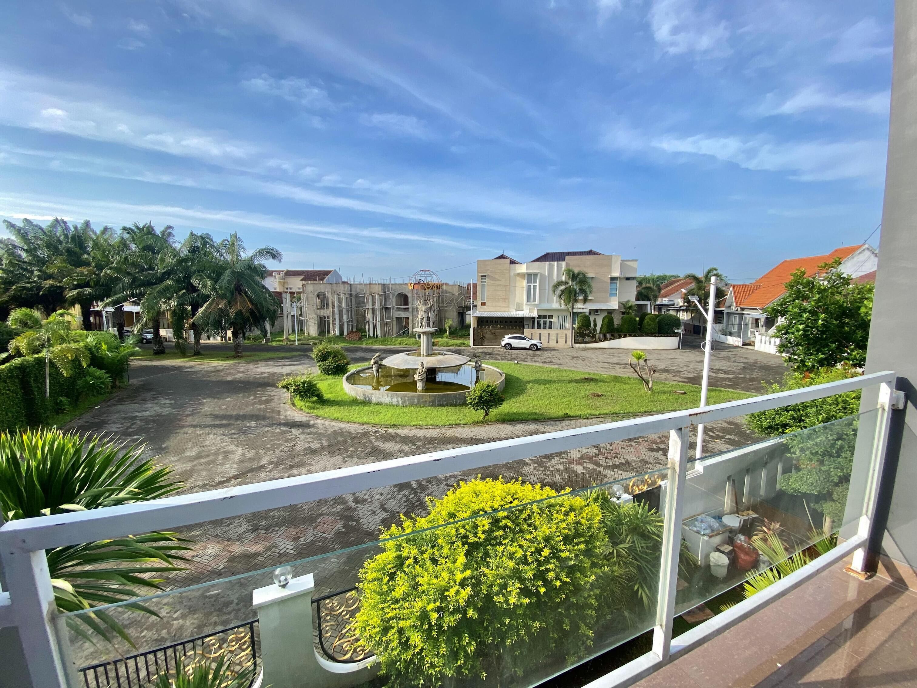 Zona residencial con una fuente central, casas circundantes y cielo despejado.