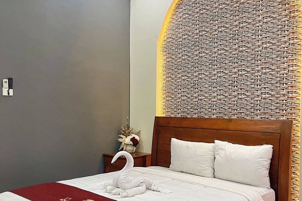 Een hotelkamer met een bed, een wandairconditioner, een decoratieve wand en een nachtkastje met een vaas.