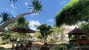 Un patio con mesa y sillas, rodeado por un borde de piedra, y un pabellón al fondo.