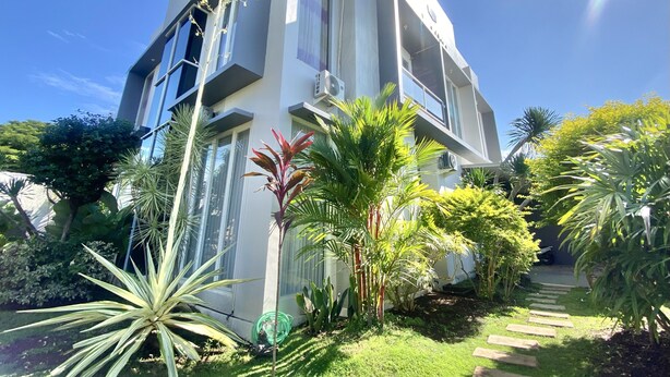 Un edificio moderno con un jardín delantero, que presenta una variedad de plantas y un camino de piedra.