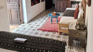 A bedroom with a wooden ceiling, a bed with patterned bedding, a small table with a lamp, and a decorative wall piece. - Riad Authentique, à Proximité de la Mer et de Tous les Sites à Visiter à Rabat (RABAT)