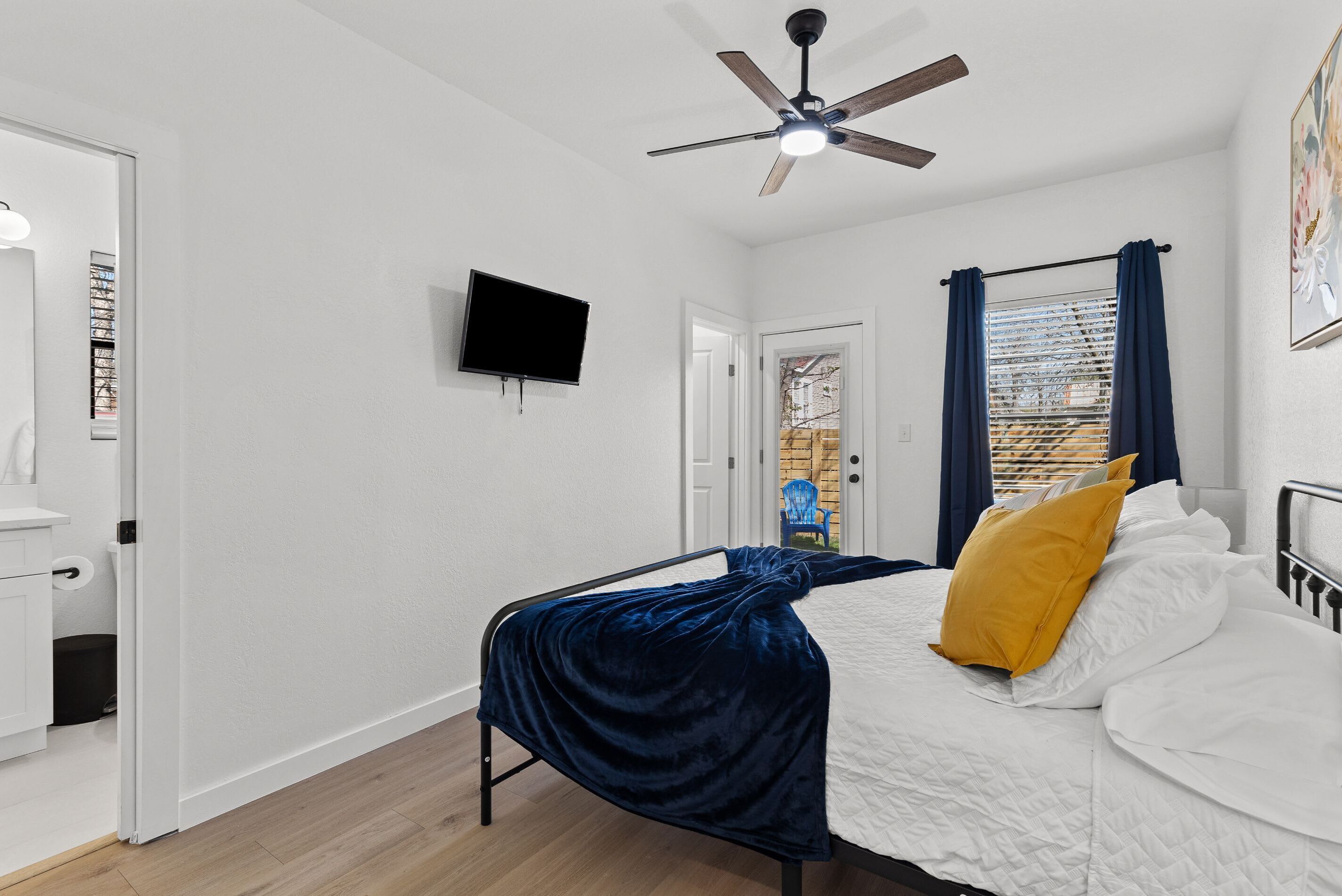 Une chambre à coucher avec un lit, un ventilateur de plafond, une télévision et une fenêtre avec des rideaux.