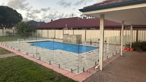 Ein Garten mit Schwimmbad, überdachter Terrasse und einem eingezäunten Bereich.