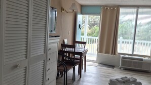 A bedroom with a bed, a desk, and a chair. There is a window with curtains and a view of trees outside. - Cute Lil' Condo on Intracoastal waterway with beach access and large pool (Atlantic Beach)