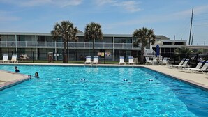 A swimming pool with clear blue water, surrounded by lounge chairs and palm trees. - Cute Lil' Condo on Intracoastal waterway with beach access and large pool (Atlantic Beach)