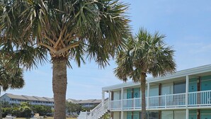 A two-story motel with a blue exterior and white railings, featuring a covered parking area and a grassy lawn with palm trees. - Cute Lil' Condo on Intracoastal waterway with beach access and large pool (Atlantic Beach)
