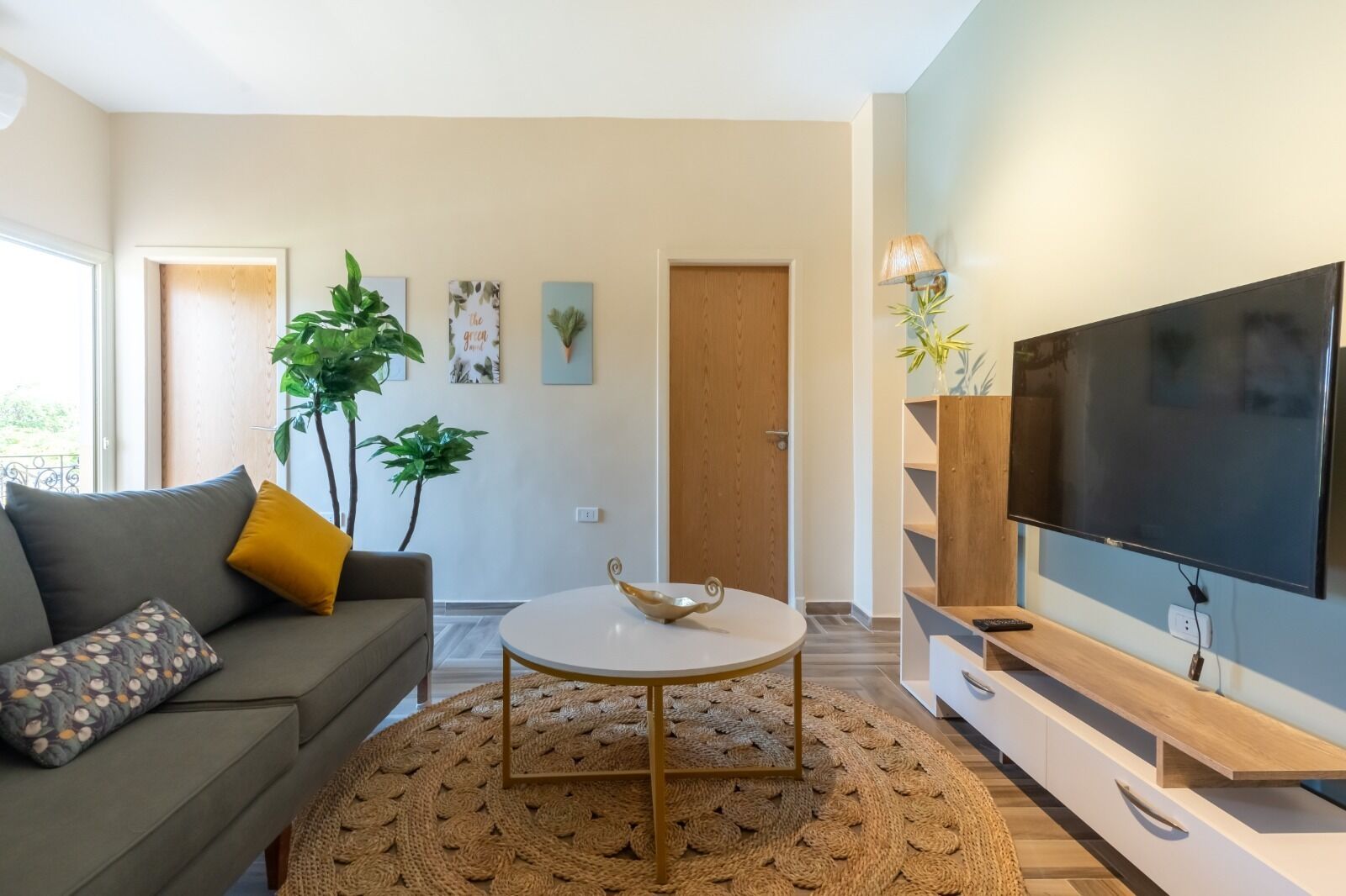 A modern living room with a sofa, a round coffee table, a TV, and decorative plants.