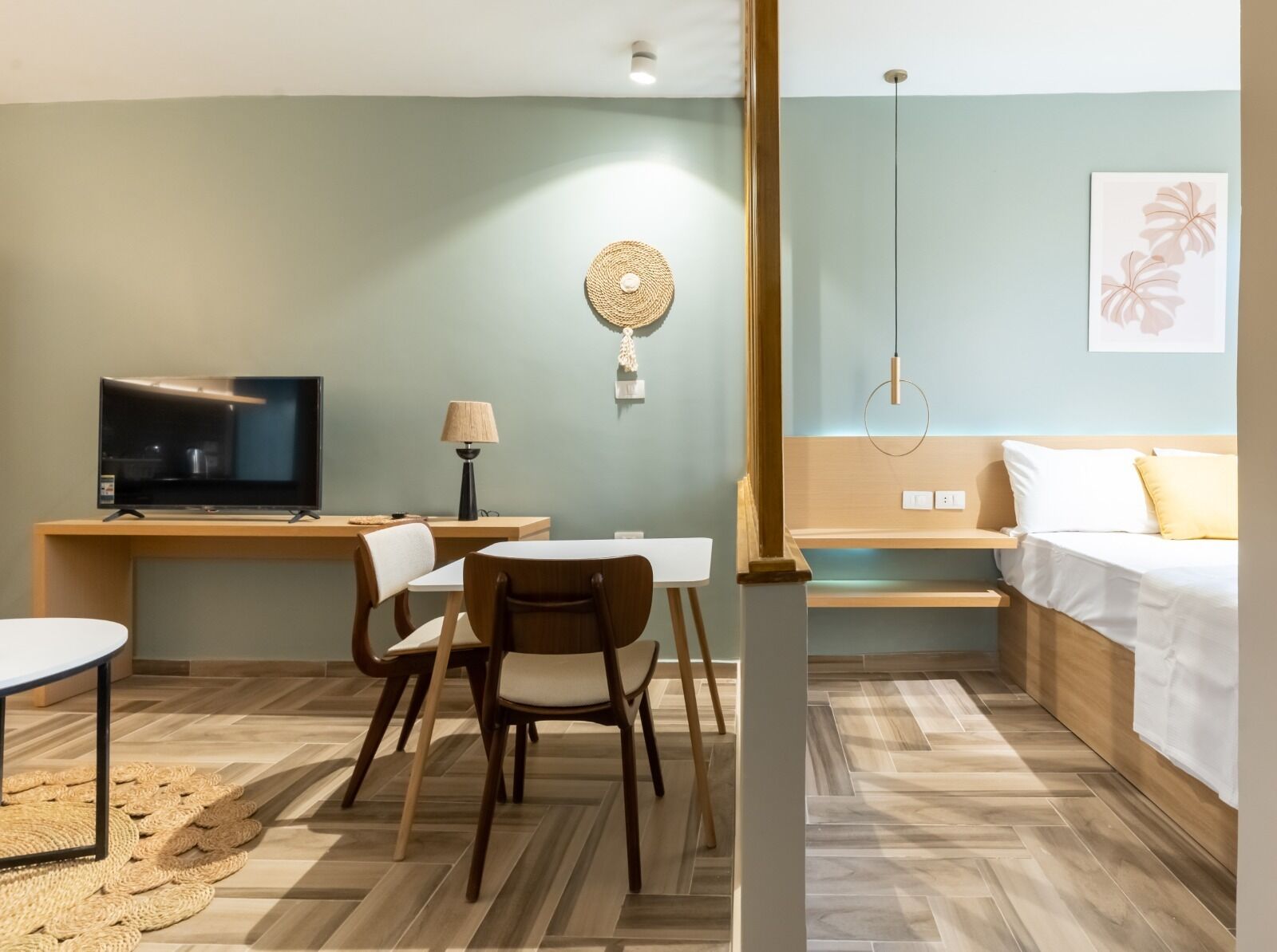 A hotel room with a bed, a desk with a TV, a chair, a lamp, and a wall-mounted light fixture.