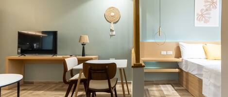 A hotel room with a bed, a desk with a TV, a chair, a lamp, and a wall-mounted light fixture.