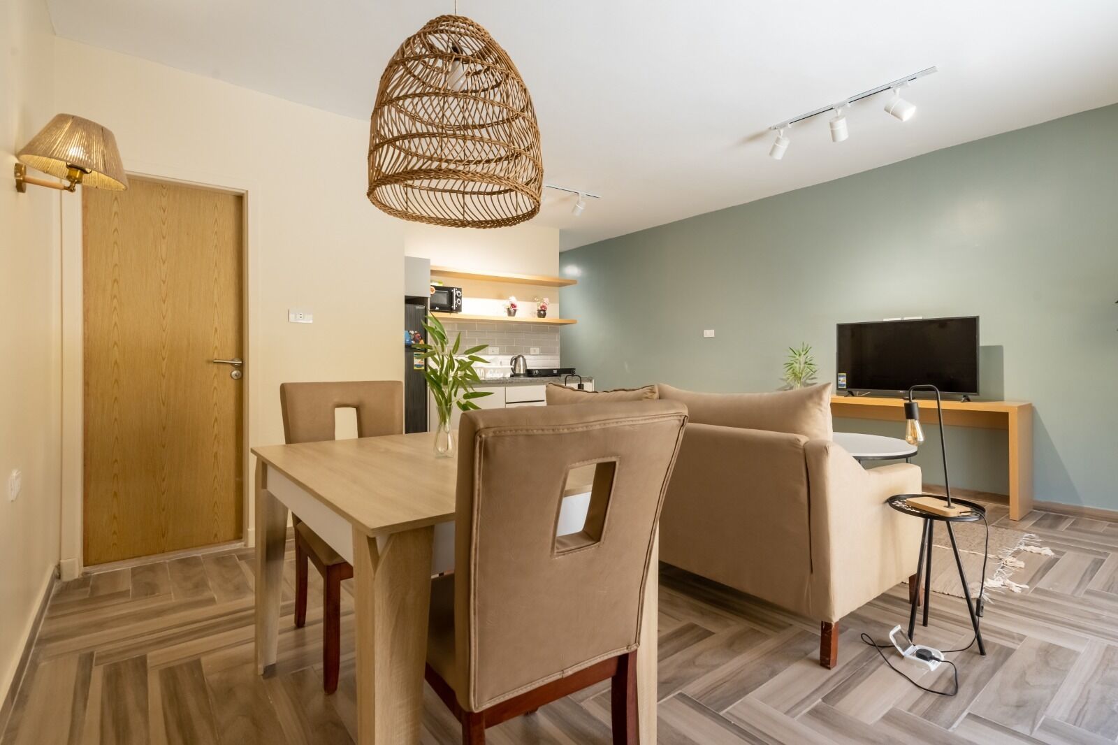 A modern living room with a dining area, a television, and a kitchen in the background.