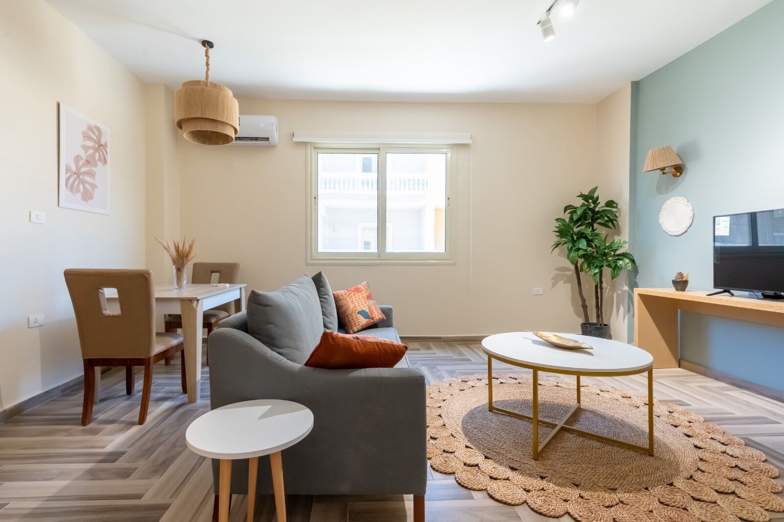 A modern living room with a grey sofa, a round coffee table, and a dining area with a table and chairs.