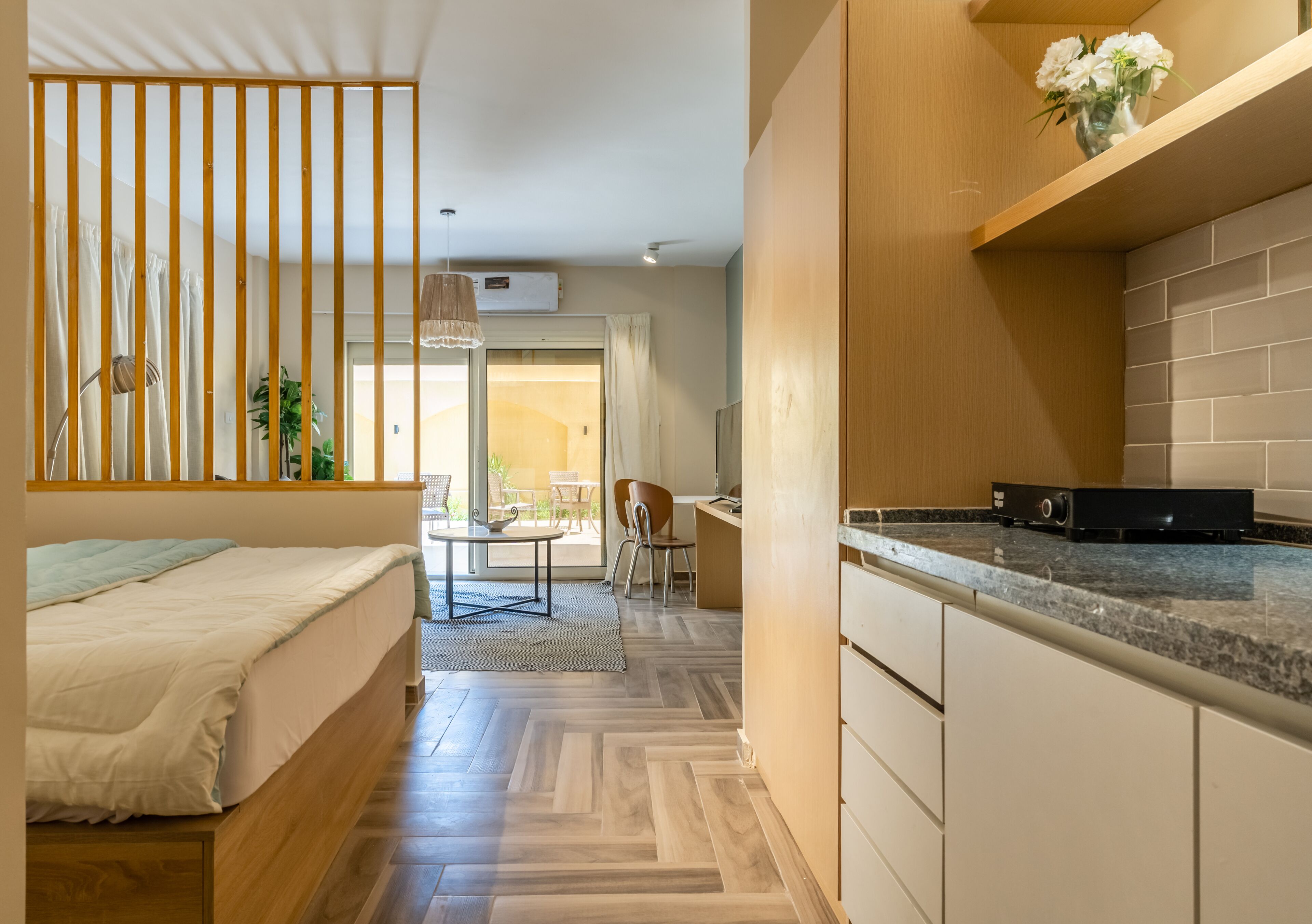 A modern bedroom with a bed, a wooden floor, a kitchen area with a countertop and cabinets, and a dining area with a table and chairs.